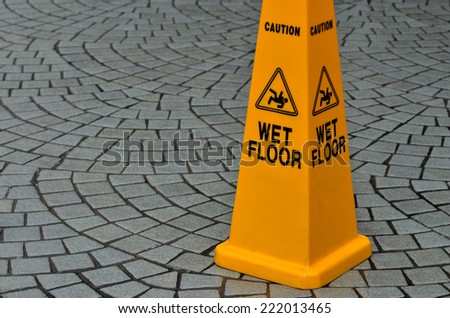 Slippery floor surface warning sign and symbol on empty city street peacock tail paving cobbles back mesh stone. Concept photo danger.No people. Copy space
