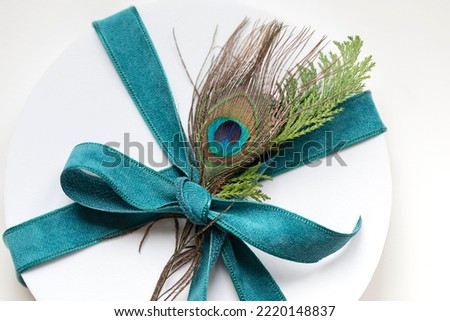 Christmas round white gift box with peacock feather top view close up. Winter holiday festive greeting card	