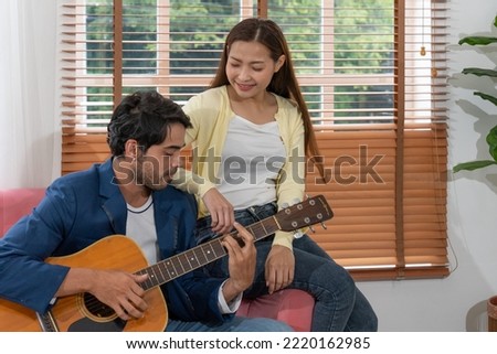 Mixed Race Couple Playing Guitar and Singing Song Together in Living Room at Home