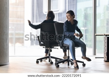 Cheerful Indian office employees, joyful colleagues have fun together at workplace, finish task successfully, enjoy break, workday end, riding seated on chairs looking overjoyed celebrate work result Royalty-Free Stock Photo #2220172091