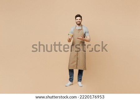 Full body young happy fun man barista barman employee wears brown apron working in bar pub hold martini glass cocktails isolated on plain pastel light beige background. Small business startup concept Royalty-Free Stock Photo #2220176953