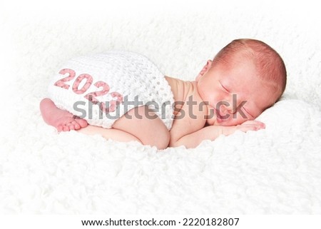 Happy New Year 2023. Newborn baby girl asleep on a white blanket.  Royalty-Free Stock Photo #2220182807