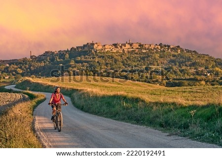 nice senior woman riding her electric mountain bike between olive trees in the Ghianti area with Montepulciano in background, Tuscany , Italy Royalty-Free Stock Photo #2220192491