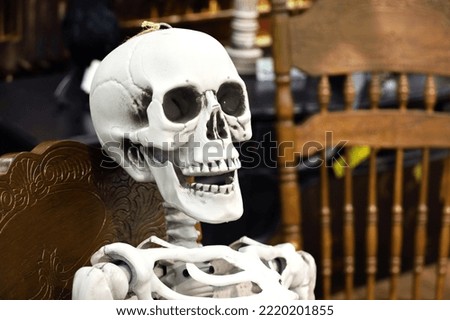 Halloween decorations, scary background. Skeleton sitting on wooden chair