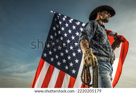 Caucasian Cowboy with American Country Flag and a Rope in His Hands Against Blue Sky