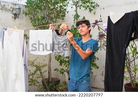 Young man does work at home, hangs clothes on clothesline. Royalty-Free Stock Photo #2220207797