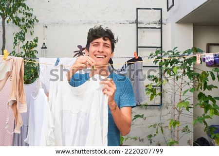 Young man does work at home, hangs clothes on clothesline. Royalty-Free Stock Photo #2220207799