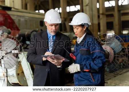 A business man inspects the work of an on-site worker at an old factory for rehearsing train engines.