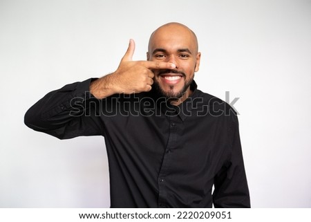 Portrait of joyful young man touching nose. Happy multiethnic male model with bald head and beard in black shirt looking at camera, laughing while teasing someone. Amusement concept Royalty-Free Stock Photo #2220209051