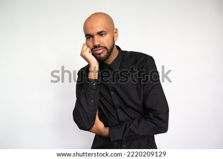 Portrait of sad young man leaning on hand. Bored multiethnic male model with bald head and beard in black shirt looking away, waiting or listening to something boring. Boredom, apathy concept