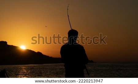 Silhouette of a standing man fishing at sunset in Turkey. Angler man holding fishing rod by the sea at evening. Leisure activity Royalty-Free Stock Photo #2220213947