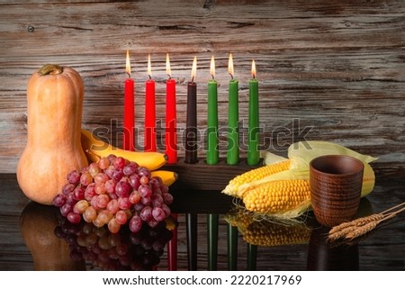 Kwanzaa holiday concept with traditional lit candles, pumpkin, corns, grapes, banana, bowl and of wheat with reflection over black background