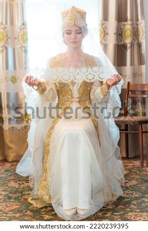 Beautiful modest uzbek bride sitting in national dress and hat and veil Royalty-Free Stock Photo #2220239395