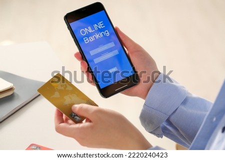 Woman using online banking app on smartphone and credit card at white office table, closeup