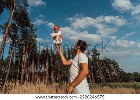 a family walks in the middle of nature with two children, twin sisters;
daughter stands on dad's hand