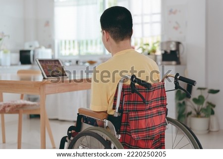 Behind of Young man with a disability using mini laptop for learning or studying with remote or Watch cartoons,Teenage boy use technology, social media, Homeschool,Hobby and education Concept.