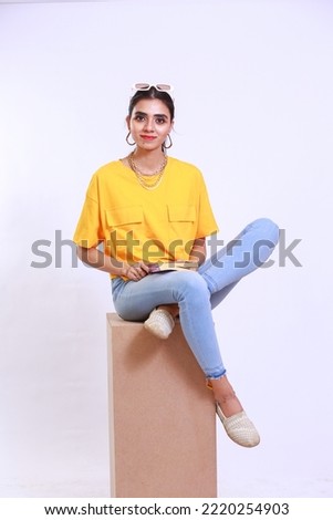 Young girl with a book sitting on a box stool, Fashionable trendy girl is wearing yellow tshirt. Isolated on a white studio background