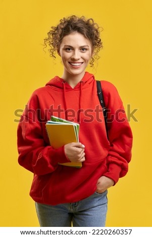 Portrait of girl with curly hair standing, smiling. Student with rucksack and curly hair looking at camera, hlding hand in pocket, wearing red khudi and jeans, Concept of youth.