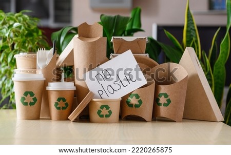 Paper eco-friendly disposable tableware with recycling signs on the background of green plants. The concept no plastic.