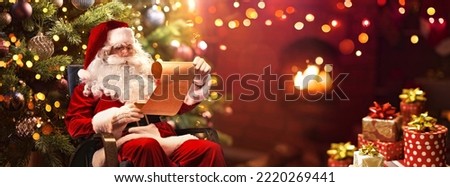 Santa Claus Sitting at His Room at Home Near Christmas Tree and Reading Christmas Letter or Wish List
