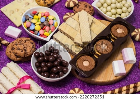 Chocolate and biscuits background. Many pieces of chocolate, candies, cookies, biscuits, cakes, donuts, and other sweets. Milk chocolate and dark chocolate, waffle coconut. Purple background Royalty-Free Stock Photo #2220272351