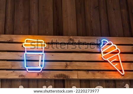 Glowing neon icons of street food, ice cream and coffee mugs on the wooden wall of a fast food restaurant.