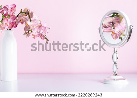 Pink orchids in vase reflected in mirror. Cosmetic dressing table. Light bathroom decor, mirror, pink orchids flowers on pink shelf. Elegant decor bathroom interior. Royalty-Free Stock Photo #2220289243