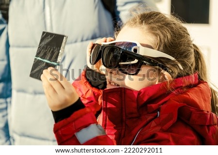 Kid watching solar eclipse with glass dark filter and several sunglasses, funny little girl looking eclipse of sun. Child viewing eclipse in sky. Concept of people, weather, science and space.  Royalty-Free Stock Photo #2220292011