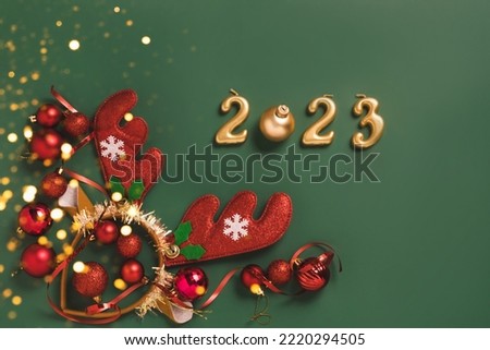 Festive layout numbers 2023, accessories New Year, wreath of horns, toys tinsel green background