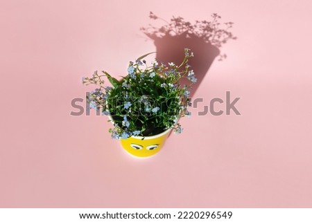 Yellow paper cup with field blue flowers on pink background.