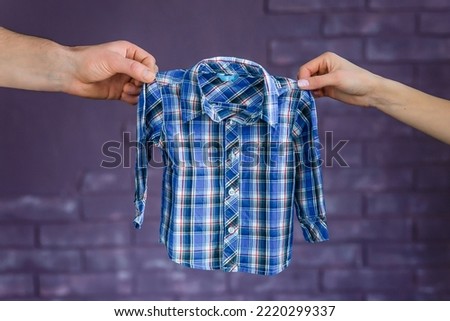 Man and woman hands hold plaid shirt on a purple background Concept waiting of baby.