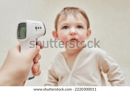 A man father measures the temperature of a sick toddler baby with a thermometer. Dad checks the high temperature of a sick child. Kid aged one year and three months