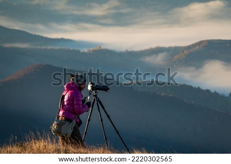 Travel photographer at work. Woman photographer with professional tripod and camera makes photos high in the mountains 