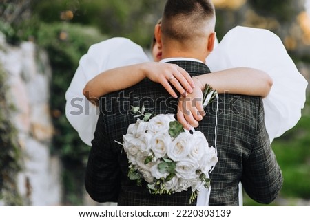 The bride hugs the groom behind his back, holding a beautiful bouquet of roses in her hands. Close-up wedding photography, portrait.