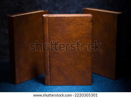 several books with the same binding on a dark background isolated. three books with a brown cover without inscriptions and titles with free space for text