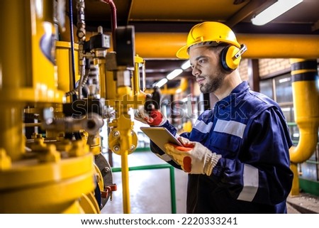 Heating plant technician standing by gas pipes and maintaining temperature inside power plant boiler room. Royalty-Free Stock Photo #2220333241