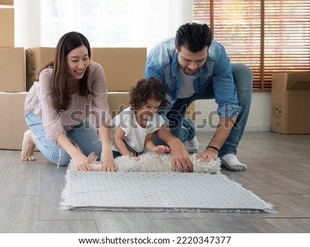 Cute little toddler girl helping mother and father rolling carpet when packing for moving house.