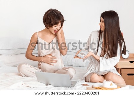 Young woman giving gift voucher to her pregnant wife in bedroom