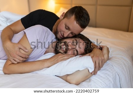 Gay couple embracing each other with their eyes closed. Two young male lovers touching their faces together while lying in bed in the morning. Affectionate young gay couple bonding at home.