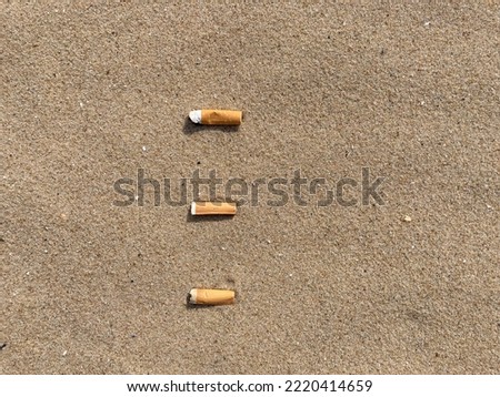 three cigarette butts arranged as bullet points in sand on beach