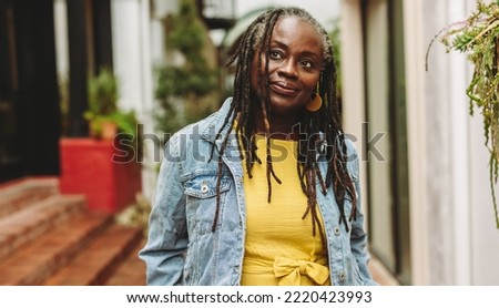 Mature woman with dreadlocks looking away thoughtfully while standing outdoors. Senior woman going out in casual clothing. Royalty-Free Stock Photo #2220423993