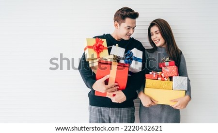 Portrait of an excited and surprised young Asian couple holding many gift boxes stacked in their hands with white background. Christmas and new year advertisement banner concept. Image with copy space