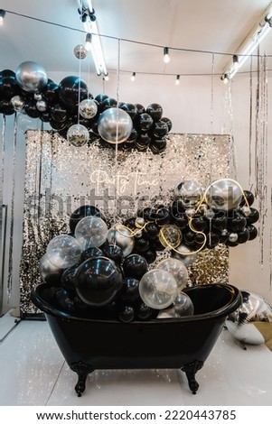 Bath for photography. Place for congratulations on birthday. Arch or photo booth decorated black and silver balloons and bulbs. Zone, wall with decor sparkling sequins for wedding. Happy New Year 2023