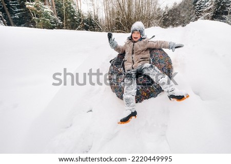 A happy boy is sitting in a tubing in the snow and riding down a slide