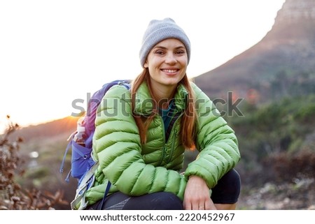 Portrait of smiling female caucasian hiker in winter clothes sitting with her dog on mountain trail in the early morning