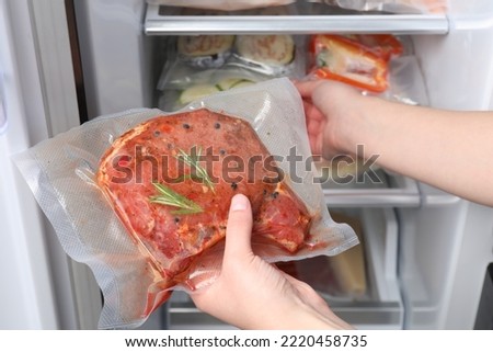 Woman putting vacuum bag with meat into fridge, closeup. Food storage Royalty-Free Stock Photo #2220458735