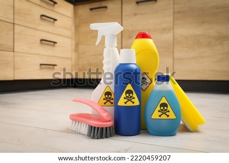 Bottles of toxic household chemicals with warning signs, scouring sponge and brush on floor indoors