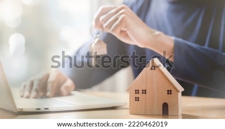 Businessman choosing mini wood house model from model and row of coin money on wood table, selective focus, Planning to buy property. 