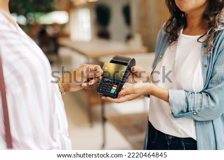 Unrecognizable ceramic store owner receiving a credit card payment from a customer in her shop. Female small business owner doing a contactless NFC transaction while serving a customer. Royalty-Free Stock Photo #2220464845
