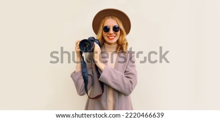 Portrait of stylish happy smiling woman photographer with digital camera taking picture wearing round hat, brown coat on background, blank copy space for advertising text